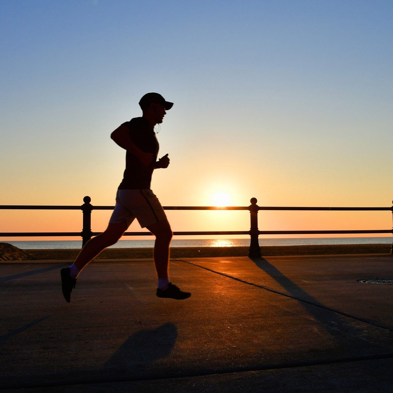 the-silhouette-of-a-male-man-runner-jogger-running-on-the-boardwalk-next-to-the-ocean-at-sunrise-or_t20_lR449g